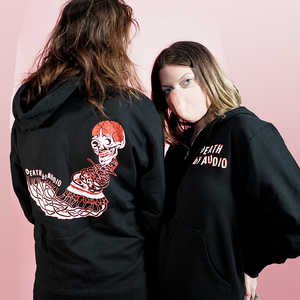 Death By Audio black hoodie shown on Oliver and Heather. Back features white and red silkscreened illustration of skull blended into Death By Audio text. Front has Death By Audio logo. 